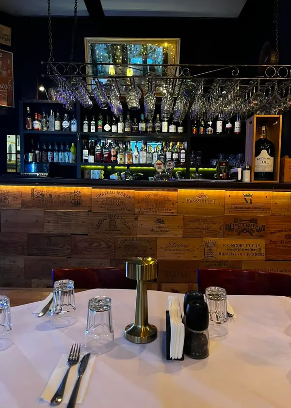 Bar z rzędem kieliszków nad ladą, na pierwszym planie nakryty stolik