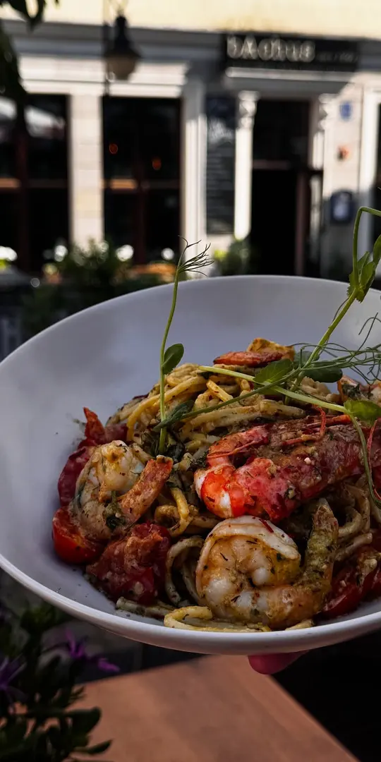 Makaron z krewetkami, w tle wejście do restauracji z szyldem bAchus